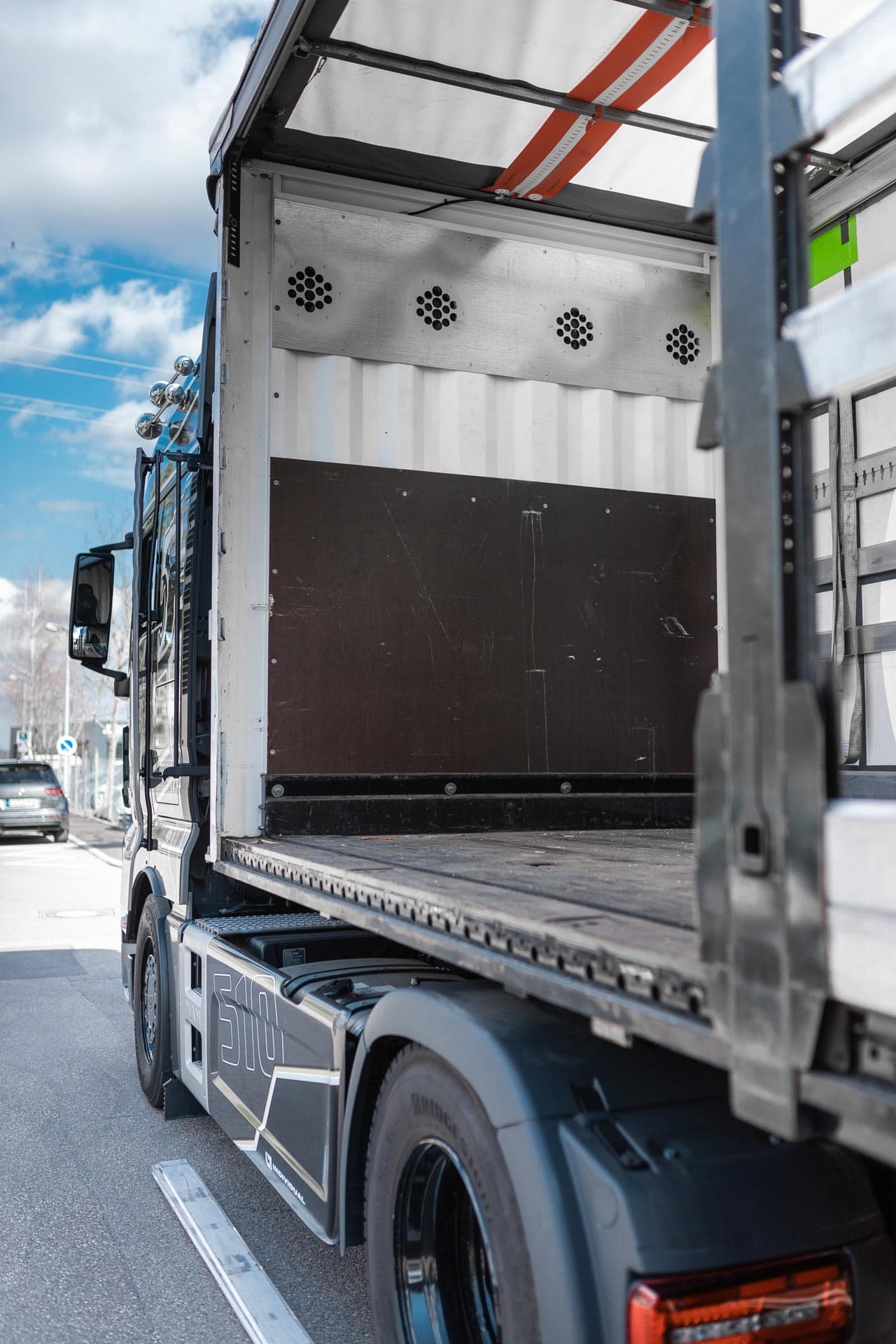 Un camion aperto con cassone argentato e pneumatici neri, parcheggiato sotto un cielo azzurro.