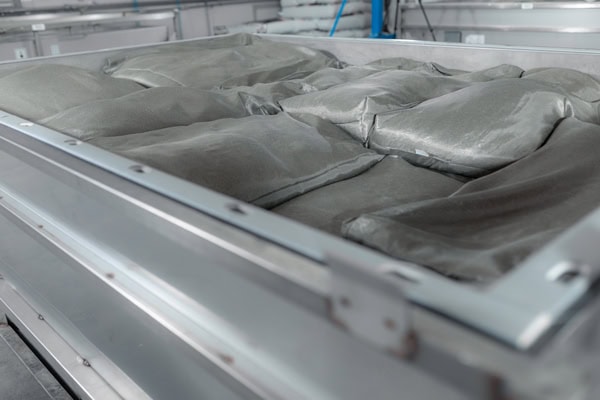Vasca industriale in acciaio inossidabile di colore grigio, piena di sacchi chiusi contenenti una polvere grigia, ricca di dettagli.