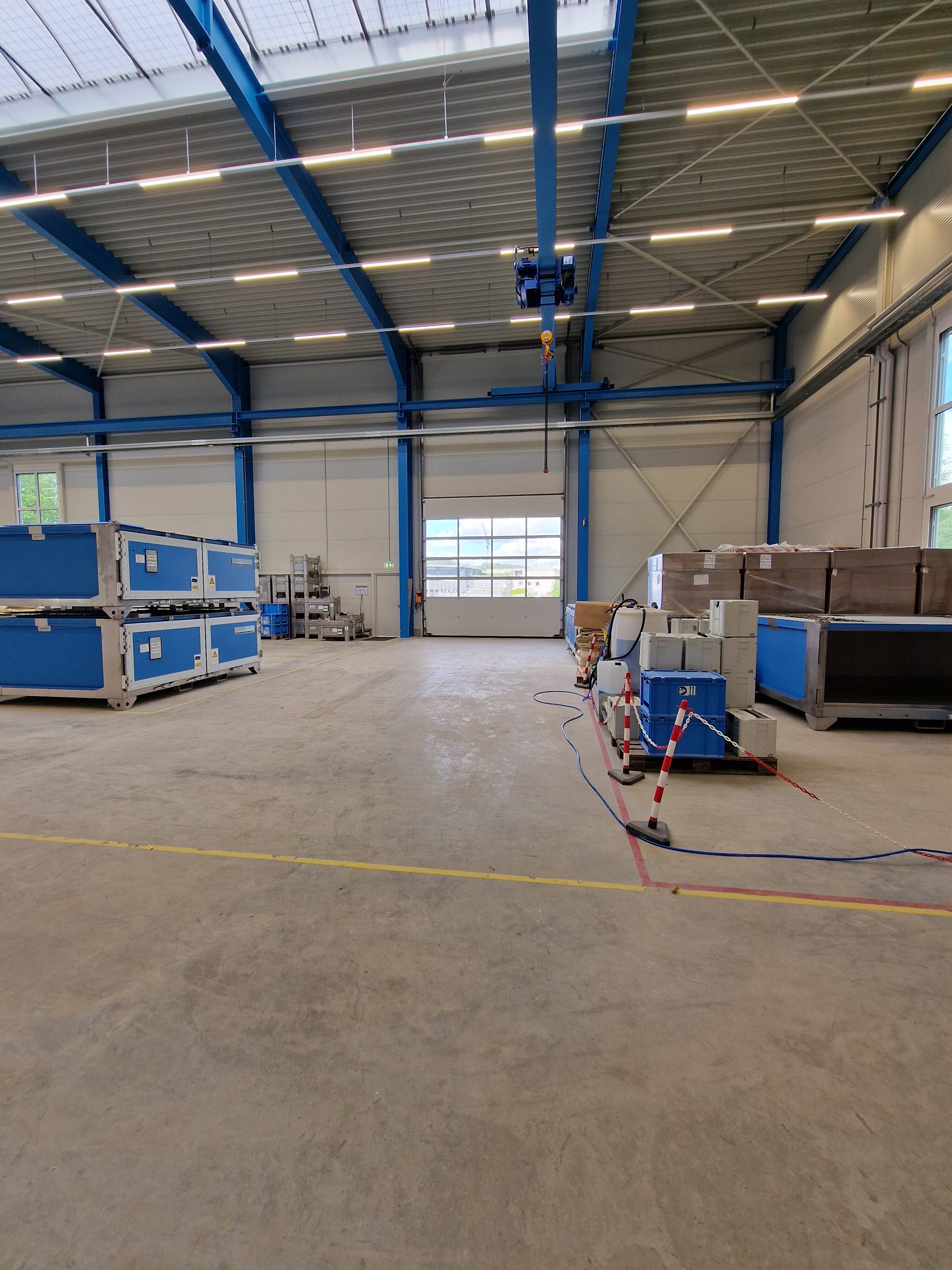 Un magazzino vuoto con scatole blu e pavimento in cemento chiaro; grandi finestre e illuminazione a soffitto.